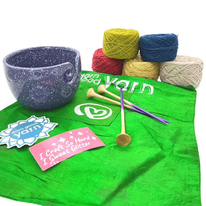DGY Ceramic Yarn bowl bundle with all items showing in front of a white background. Purple speckled ceramic yarn bowl, dgy sticker pack, US8/5mm knitting needle and crochet hook set, and dk herbal dyed yarn pack in adirondack chair colorway.