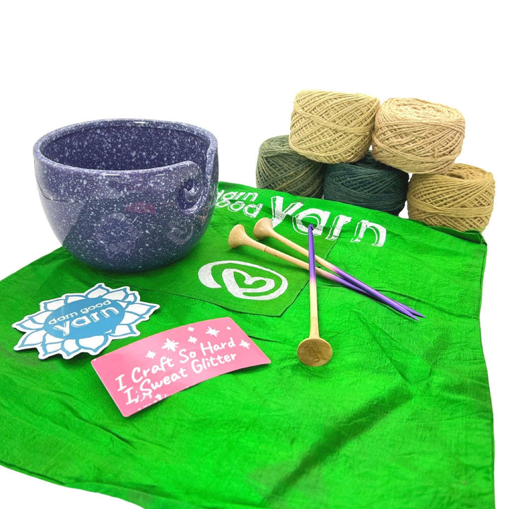DGY Ceramic Yarn bowl bundle with all items showing in front of a white background. Purple speckled ceramic yarn bowl, dgy sticker pack, US8/5mm knitting needle and crochet hook set, and dk herbal dyed yarn pack in fields of green colorway.