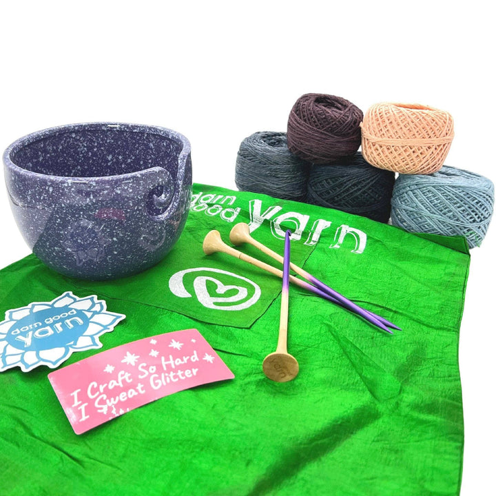 DGY Ceramic Yarn bowl bundle with all items showing in front of a white background. Purple speckled ceramic yarn bowl, dgy sticker pack, US8/5mm knitting needle and crochet hook set, and dk herbal dyed yarn pack in maine coastline colorway.