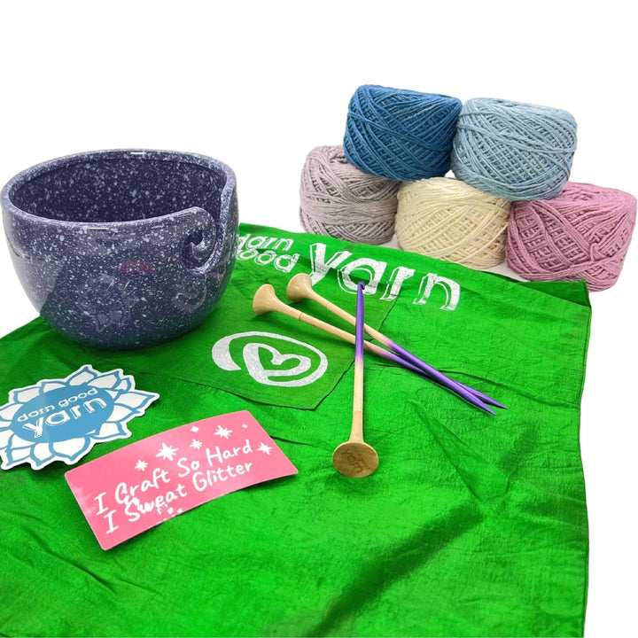 DGY Ceramic Yarn bowl bundle with all items showing in front of a white background. Purple speckled ceramic yarn bowl, dgy sticker pack, US8/5mm knitting needle and crochet hook set, and dk herbal dyed yarn pack in winter frost colorway.