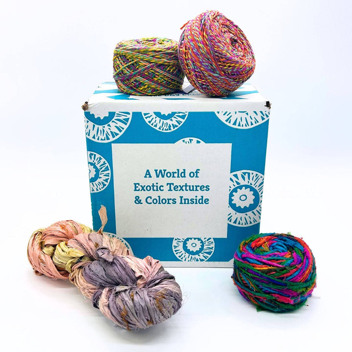 Darn Good Yarn Editor's Box mystery yarn box pictured with Darn Good Twist recycled Silk, Recycled Sari Silk Ribbon Chunky yarn, and silk roving worsted weight yarn.