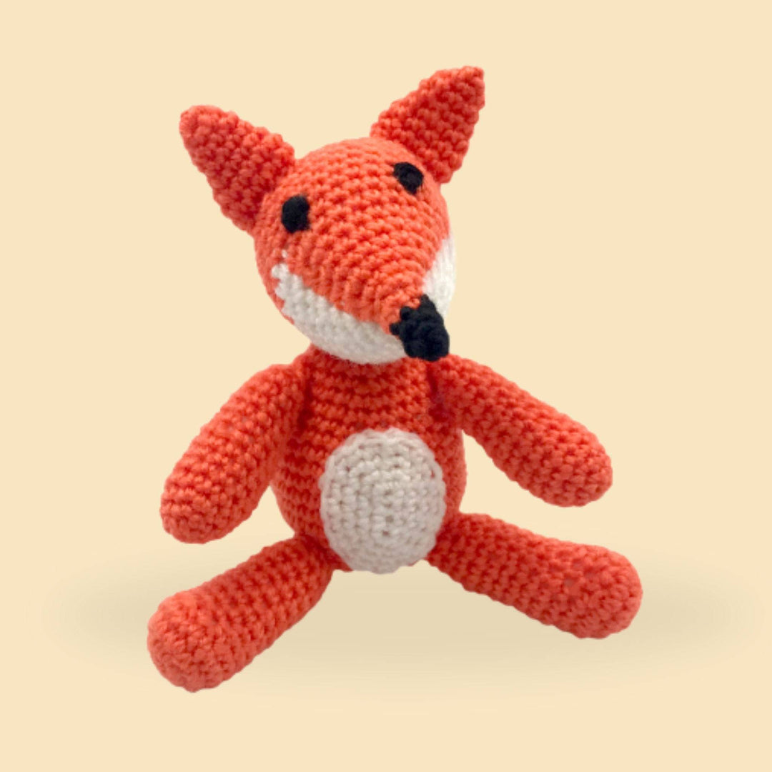 A crochet fox amigurumi plush sitting on an orange background.