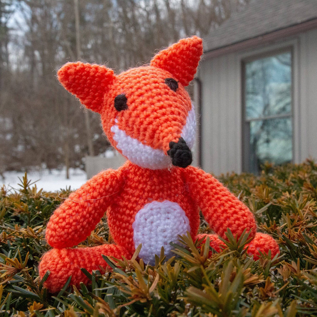 Orange crocheted fox amigurumi stuffed animal sitting on a bush