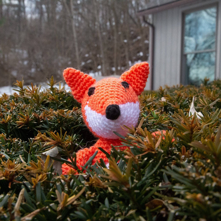 Orange crocheted fox amigurumi stuffed animal sitting in a bush
