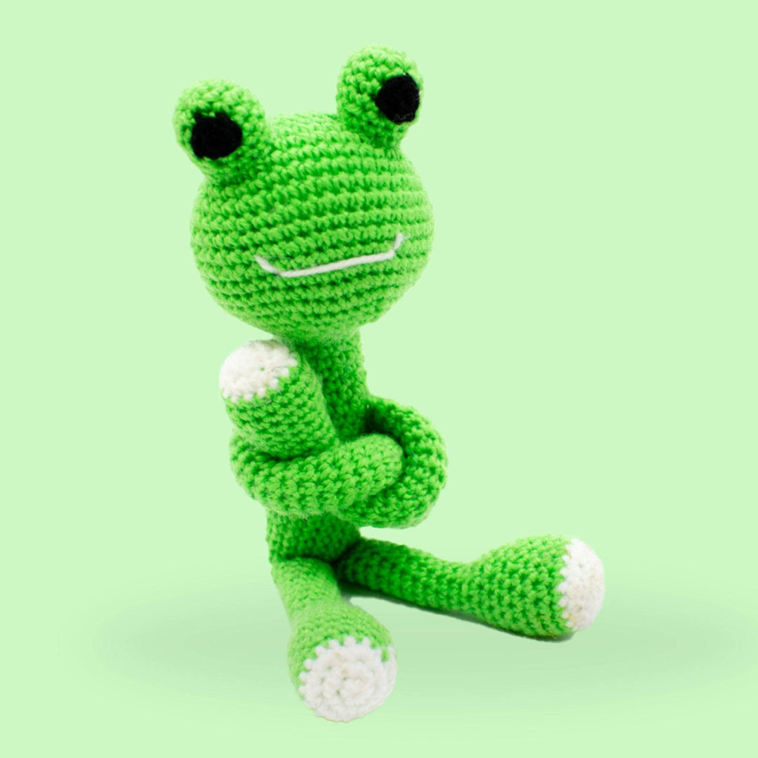 A crochet frog amigurumi plush sitting on a green background.
