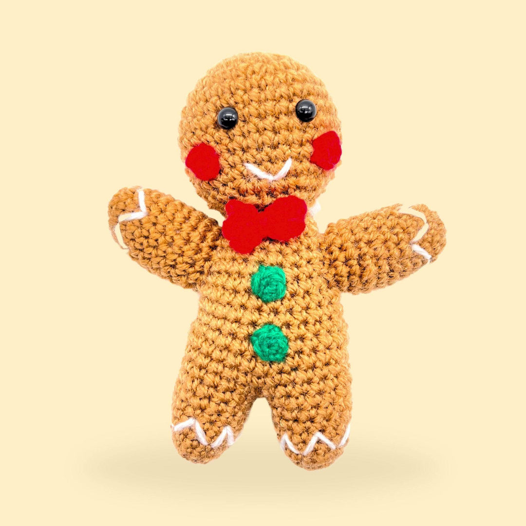 A completed crochet gingerbread man Amigurumi stuffed animal sitting on a yellow background.