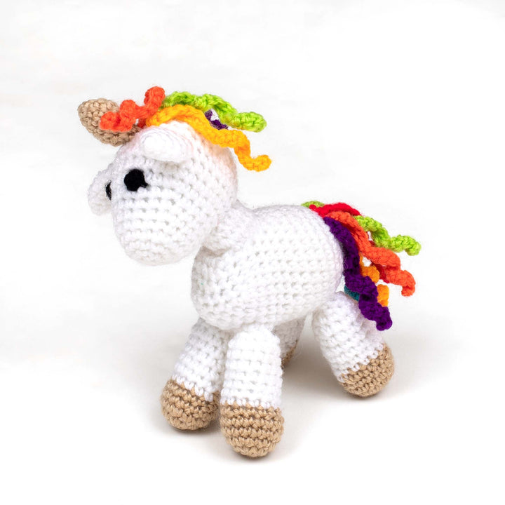 Amigurumi unicorn (white with beige accents, black eyes, and rainbow mane & tail) standing in front of a white background.