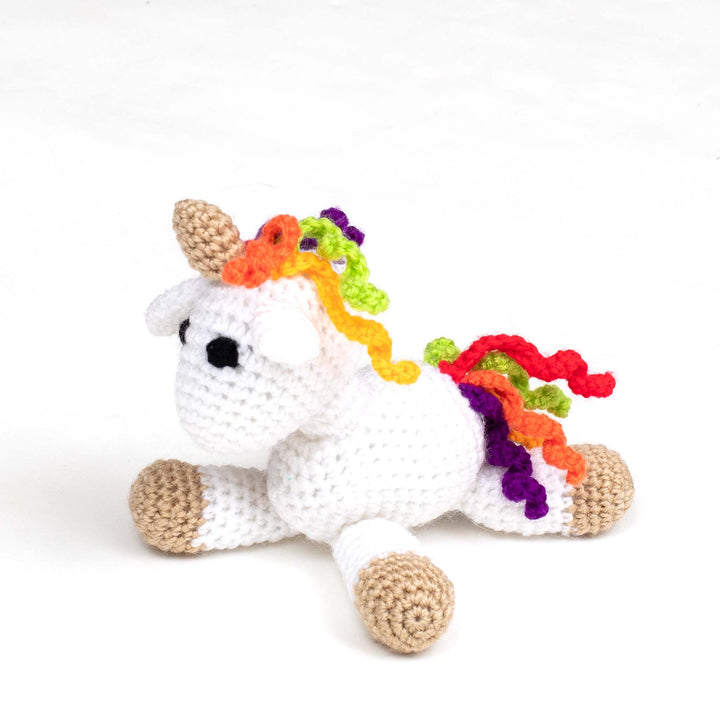 crochet unicorn amigurumi laying in front of a white background.