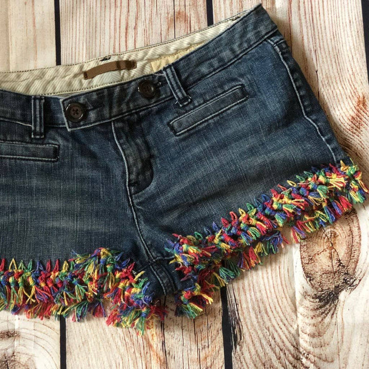Jean shorts with rainbow fringe laying on a wooden table.