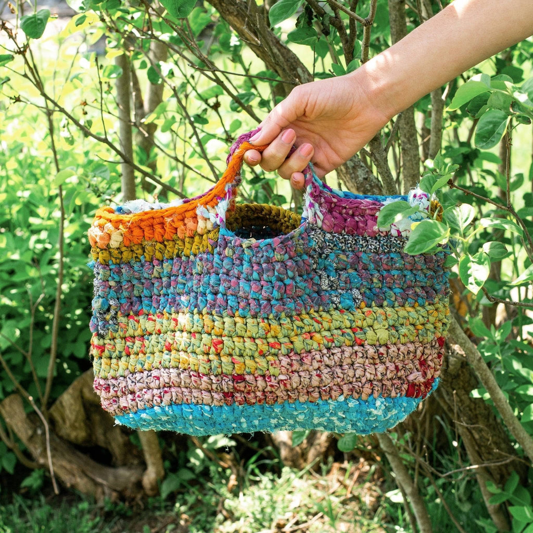 One of a kind reclaimed chiffon ribbon yarn market tote being held with greenery in the background.