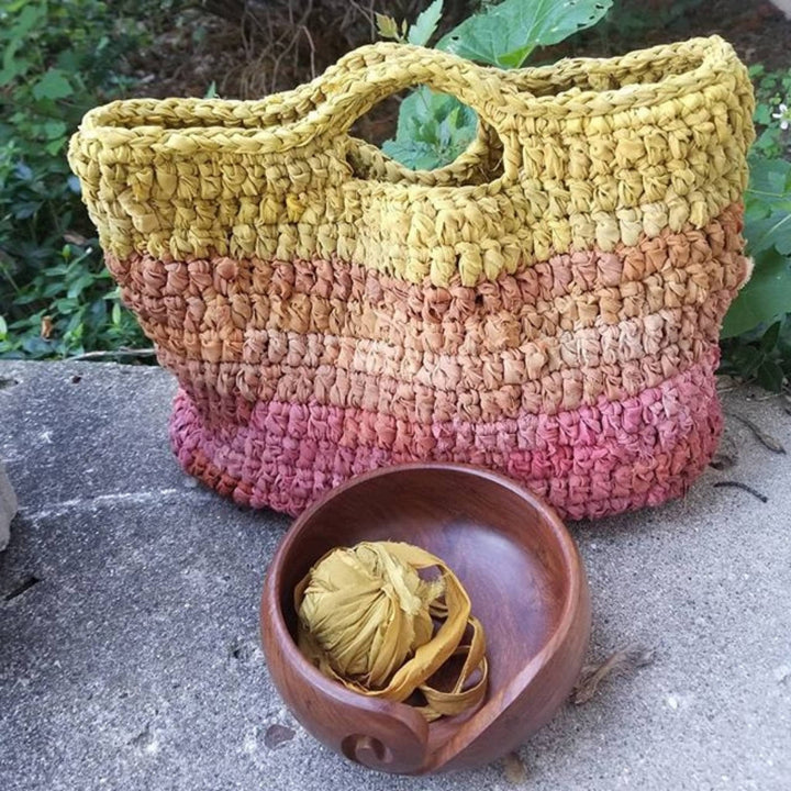 crochet version of recycled chiffon ribbon market tote in bonfire with stone and greenery in the background.