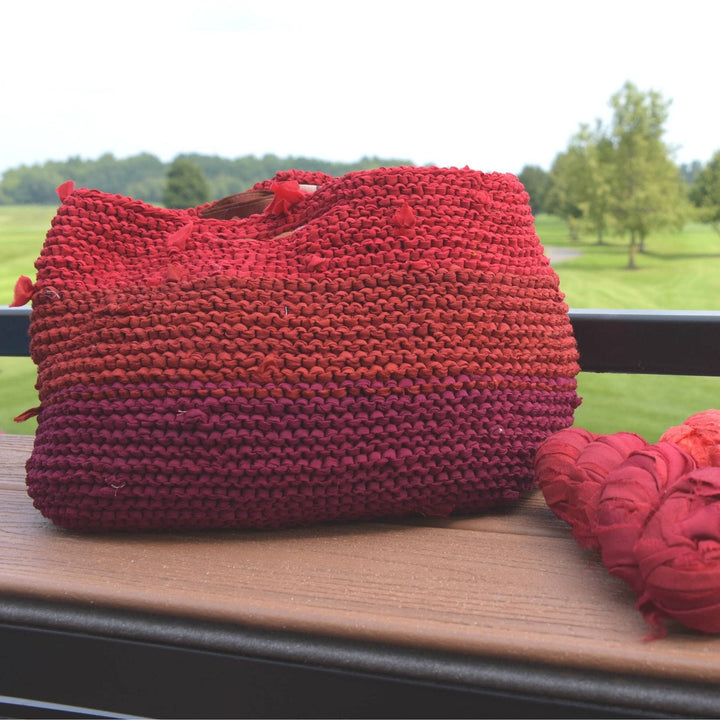 knit red market tote made from recycled chiffon ribbon yarn with greenery in the background.