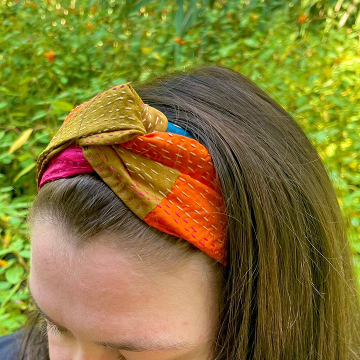 An upclose shot of a kantha stitched headband. This headband is fall colors, warm oranges and reds.