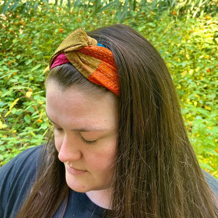 An upclose photo of a woman looking down while she's outside. She's wearing a kantha stitched headband in her long brown hair.