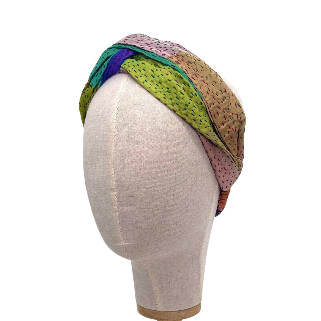 A mannequin head in front of a white background wearing a cool tone colored kantha stitched headband.