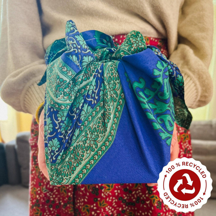 A woman in a sari wrap skirt holding a present wrapped in a blue and green sari silk furoshiki wrap.