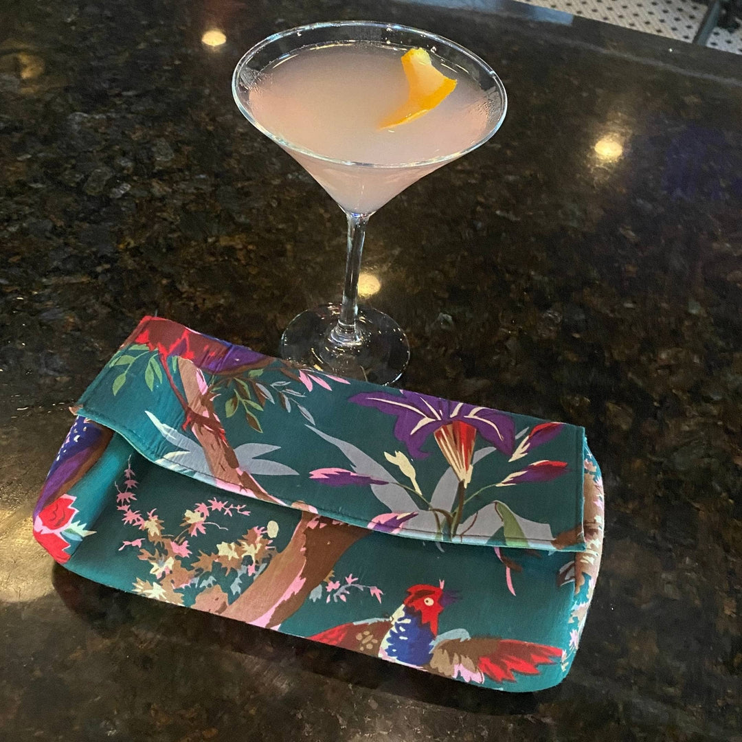 Teal clutch is sitting on a bar next to a pink cosmo. .