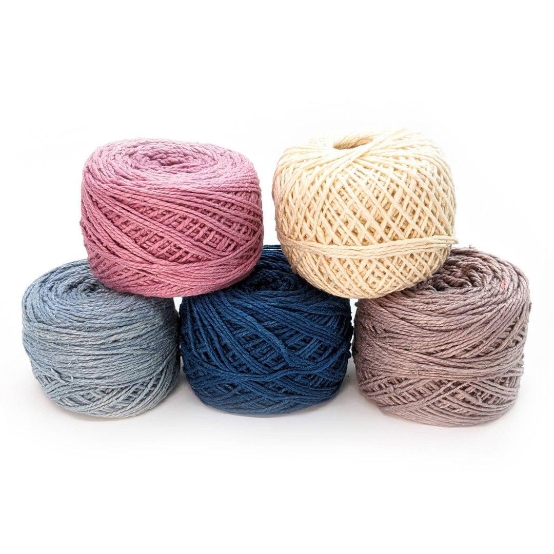 5 cakes herbal dyed reclaimed silk yarn in blues, pink, white and grey in front of a white background.