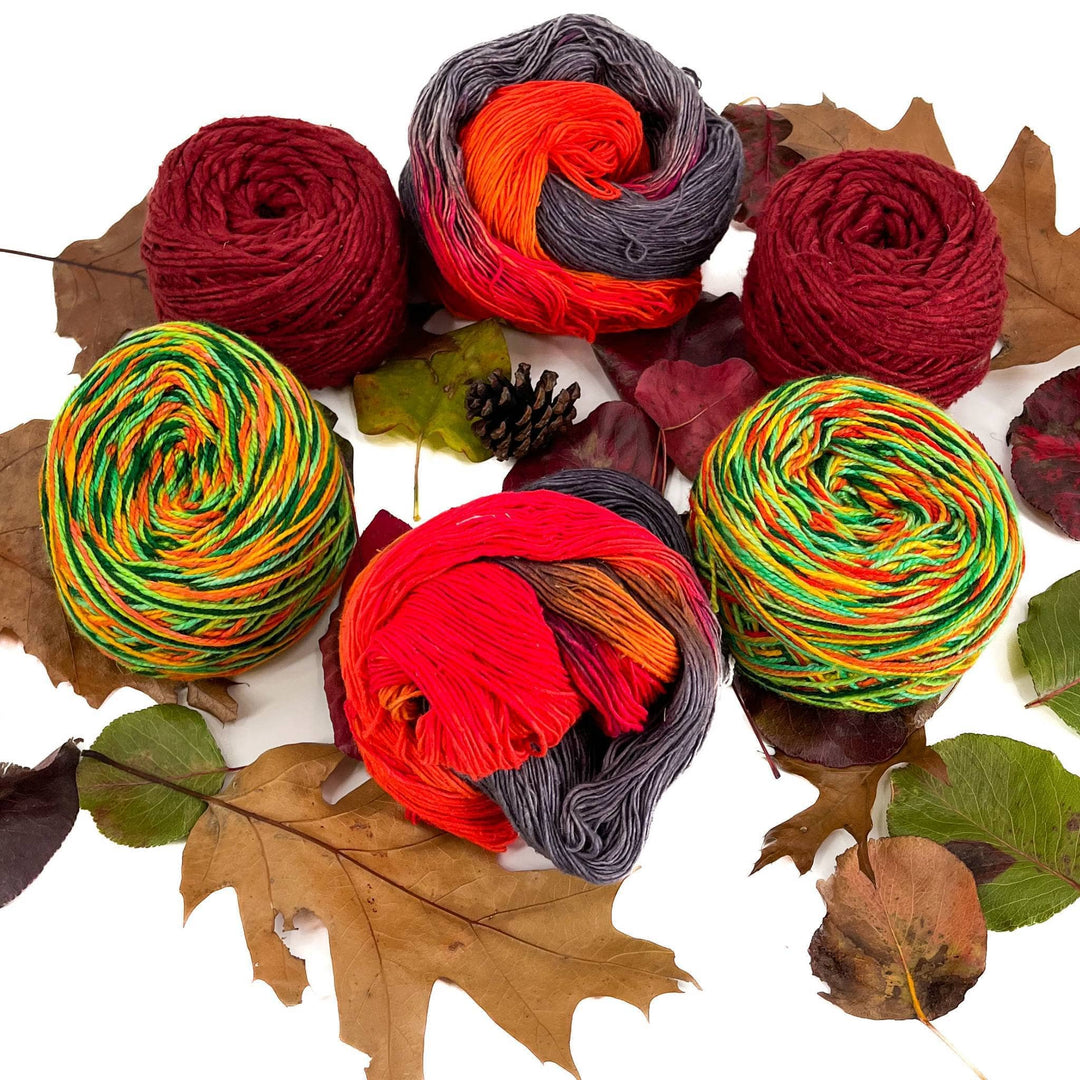 6 skeins of recycled silk yarn on a white background with leaves. All yarn is of autumn time shade and hues