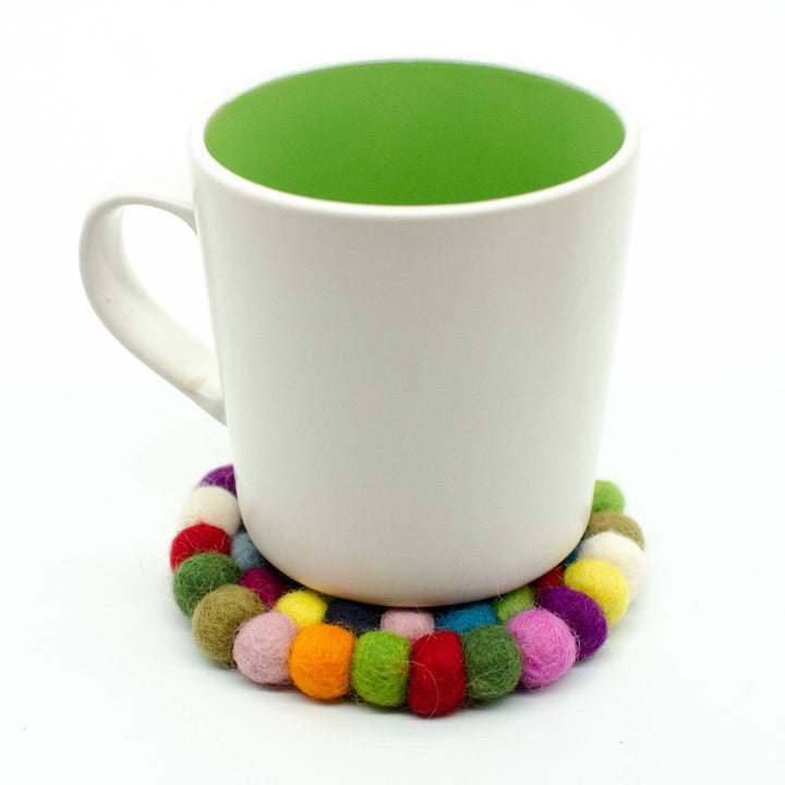 Mug sitting on top of a felt ball coaster in front of a white backdrop