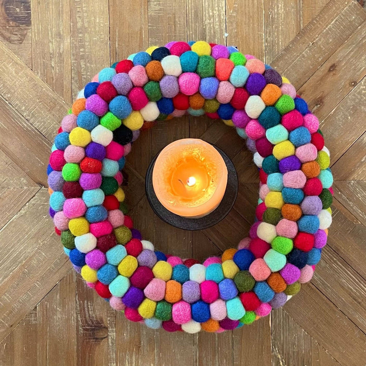 An overhead view of the felt ball wreath as a centerpiece on a table. There's a lit candle in the center to make it more decorative 