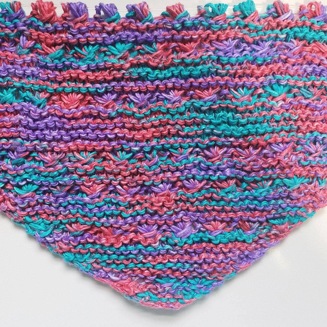 A pink, teal and blue shawl laying flat on a white background