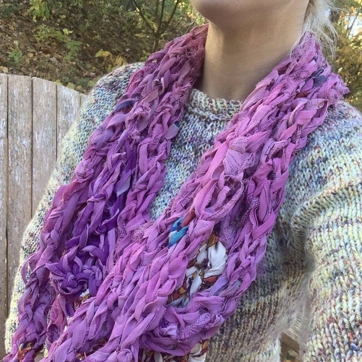 Model wearing pink finger knit infinity scarf with sweater while outside.