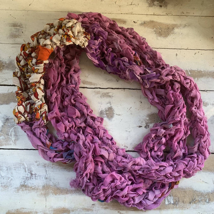 Finger knit infinity scarf in pink in front of distressed wood background.