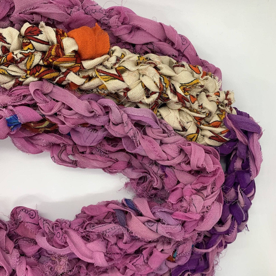 Close up image of pink finger knit infinity scarf in front of a white background.