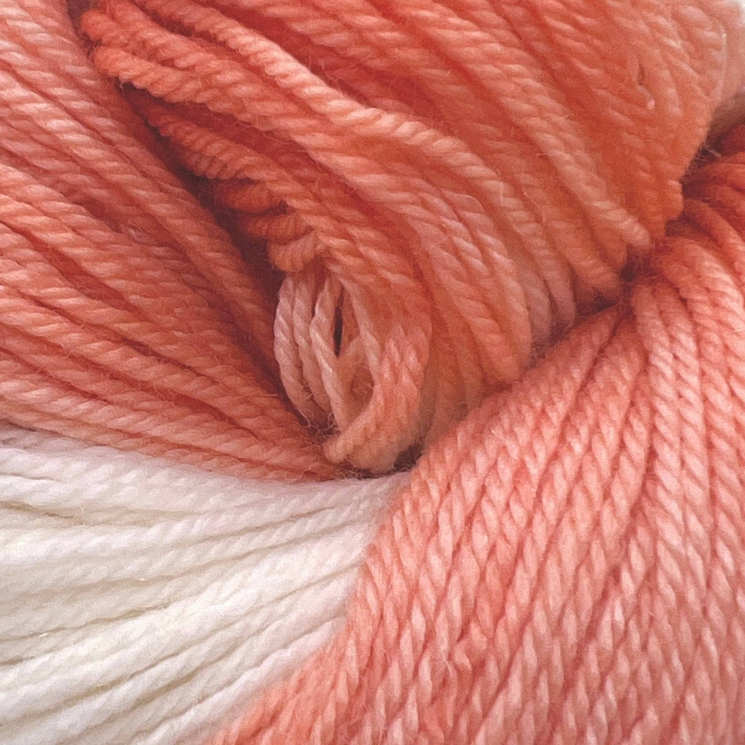 Detailed picture of light orange and white yarn on a white background. Fingering Weight Superwash Merino Wool Blended Yarn.