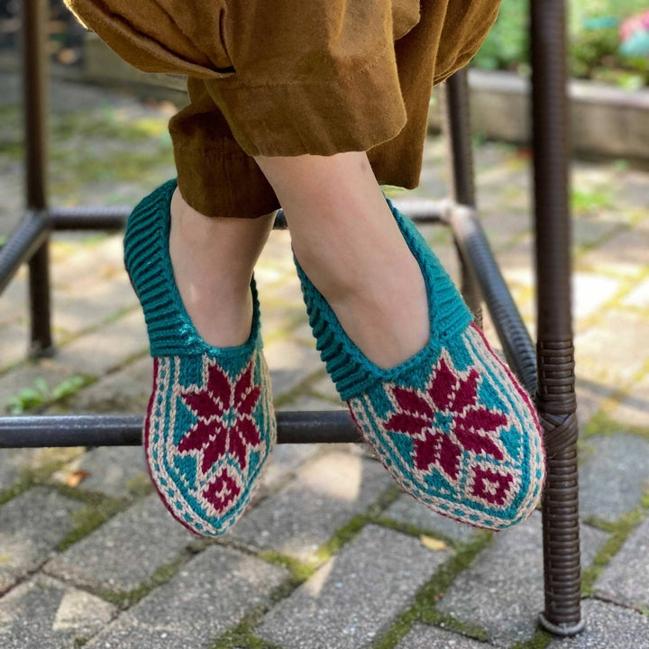 Model wearing handmade blue, burgundy and cream slippers sitting on a chair outside