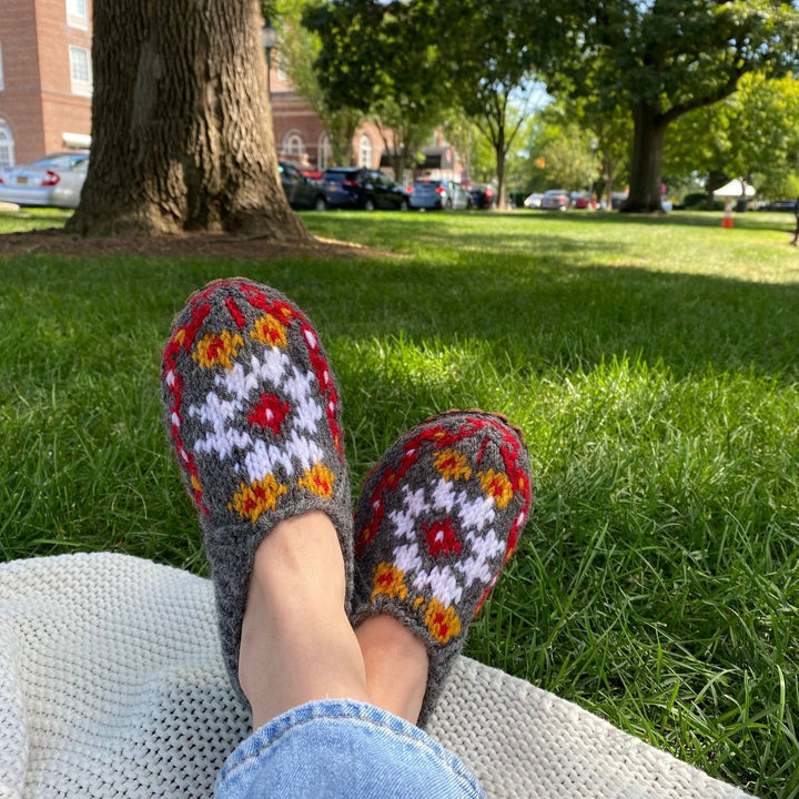 Model is wearing hand knit Folklore slippers in color Blooming Bouquet while sitting on a blanket in the park. 