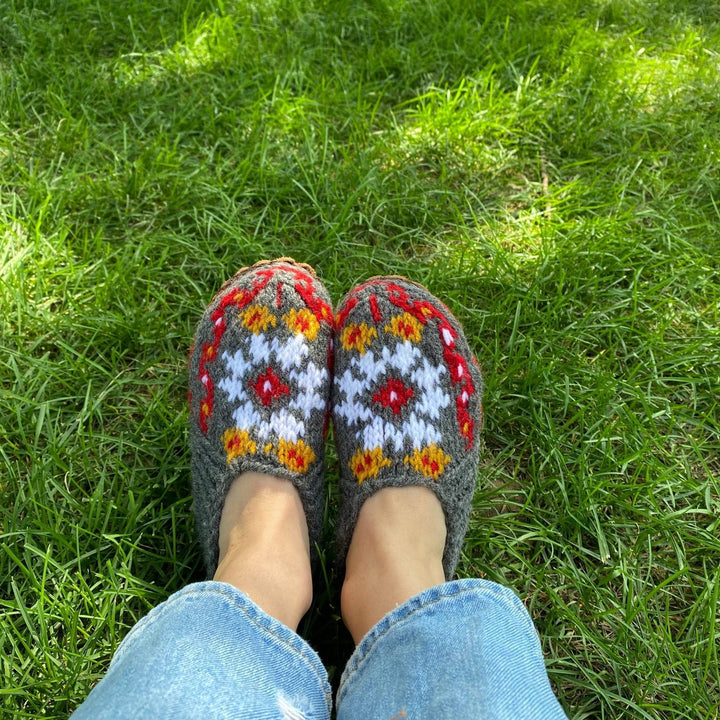 Model has their feet in the grass wearing folklore handmade slippers in color blooming bouquet 