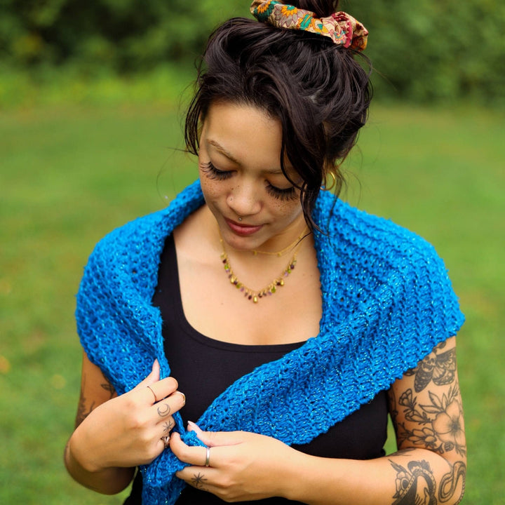 Model is looking down as she wears a blue french hen shawl. 