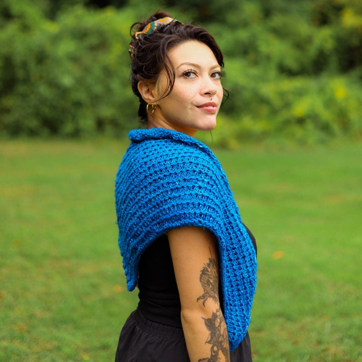Model is standing to the side wearing a blue french hen shawl. 