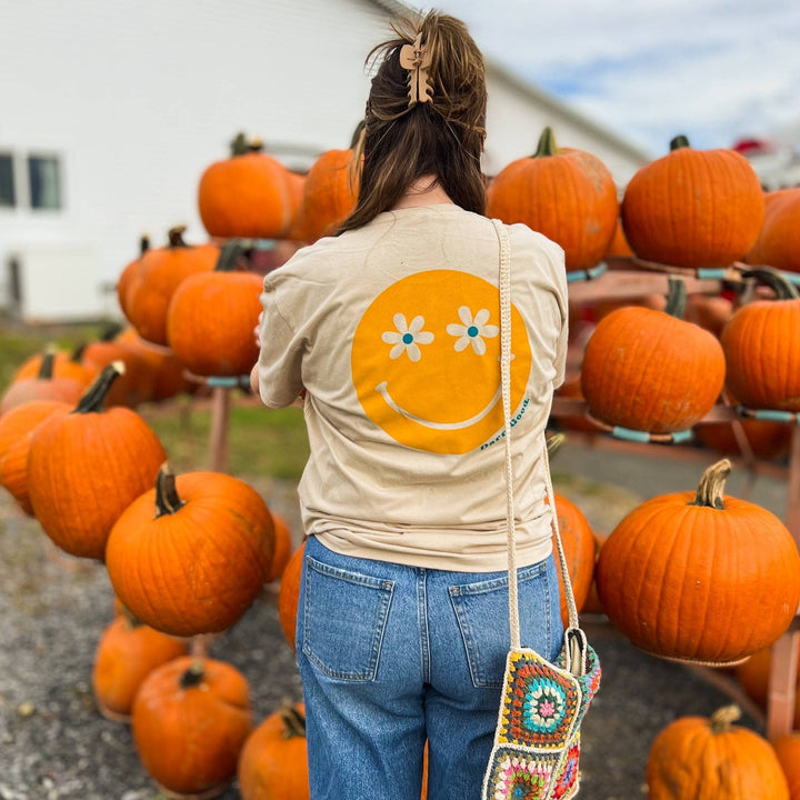 Back of model wearing a good vibes shirt with smiley face on it while standing in front of pumpkins. 