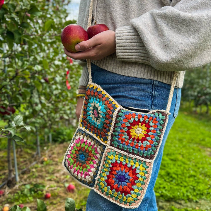 Lower half of model with a granny square bag and holding two apples. 