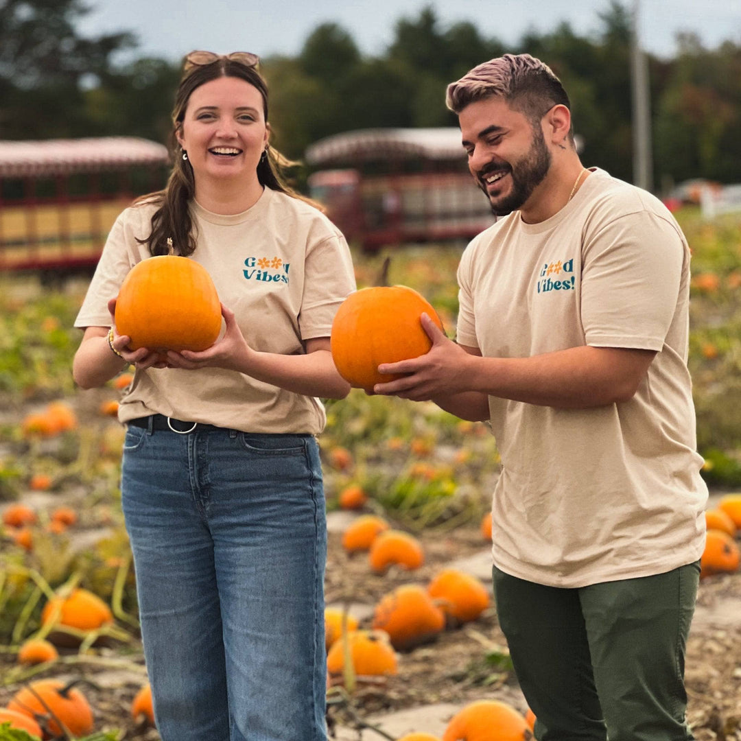Two models standing in a pumpkin patch wearing the good vibes shirt. 