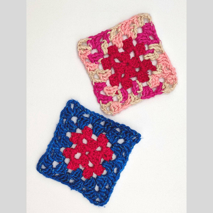 2 multi colored granny squares in front of a white background. Left to right, granny square with bright pink center and sparkly blue border. Granny square with light blue center and variegated link and white boarder.