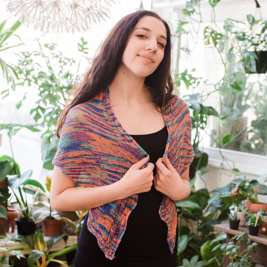 Model wearing hand beaded silk shawl knit kit in party with potted greenery in the background.