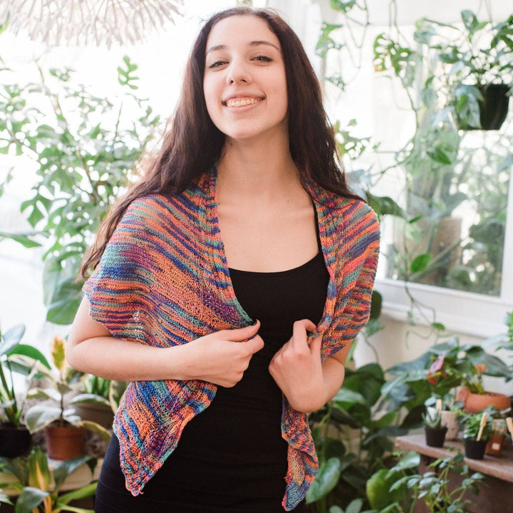 Model wearing hand beaded silk shawl knit kit in party with potted greenery in the background.