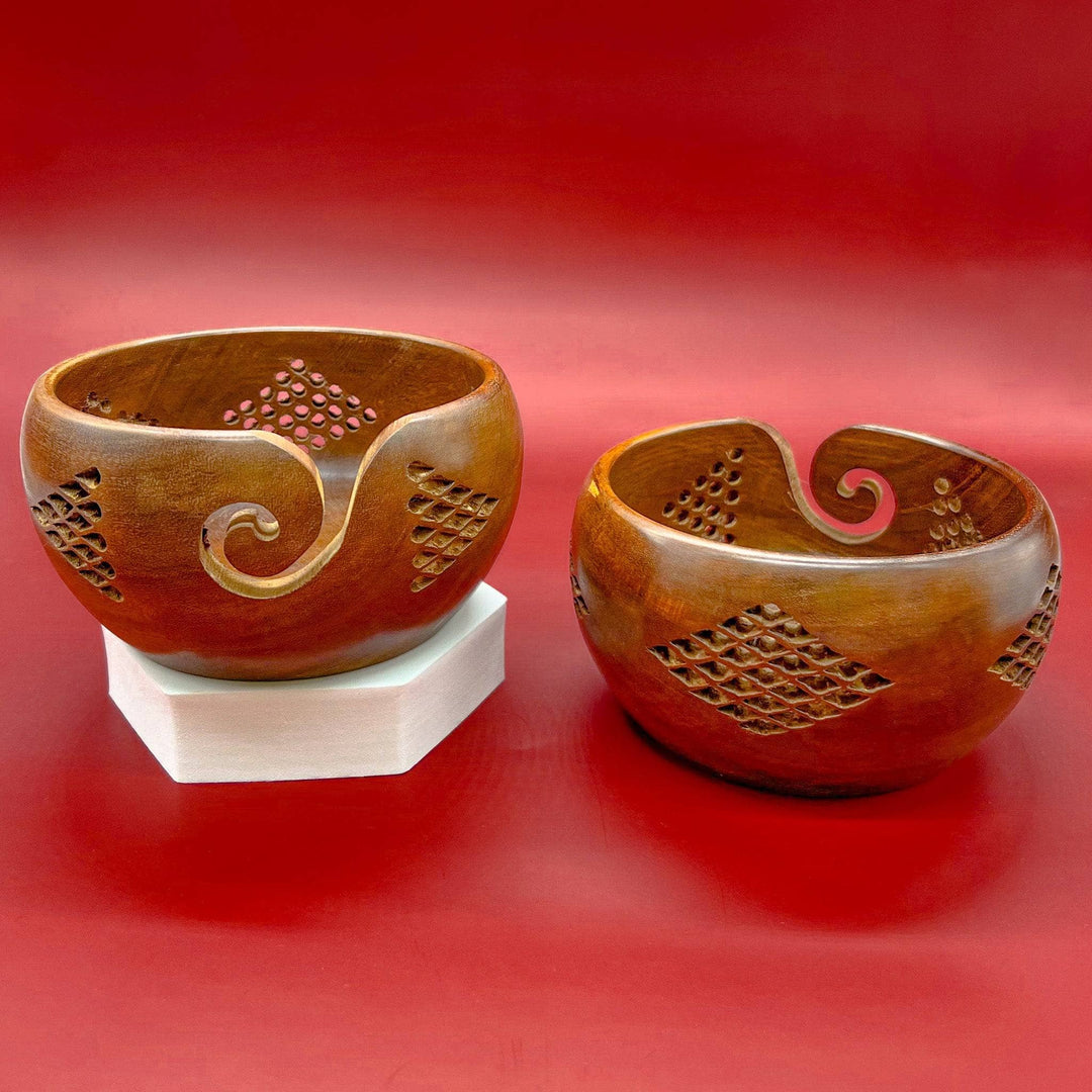 2 geometric wooden yarn bowls in front of a red background. Left YB is facing forward on octagonal white pedestal, right bowl is facing back.