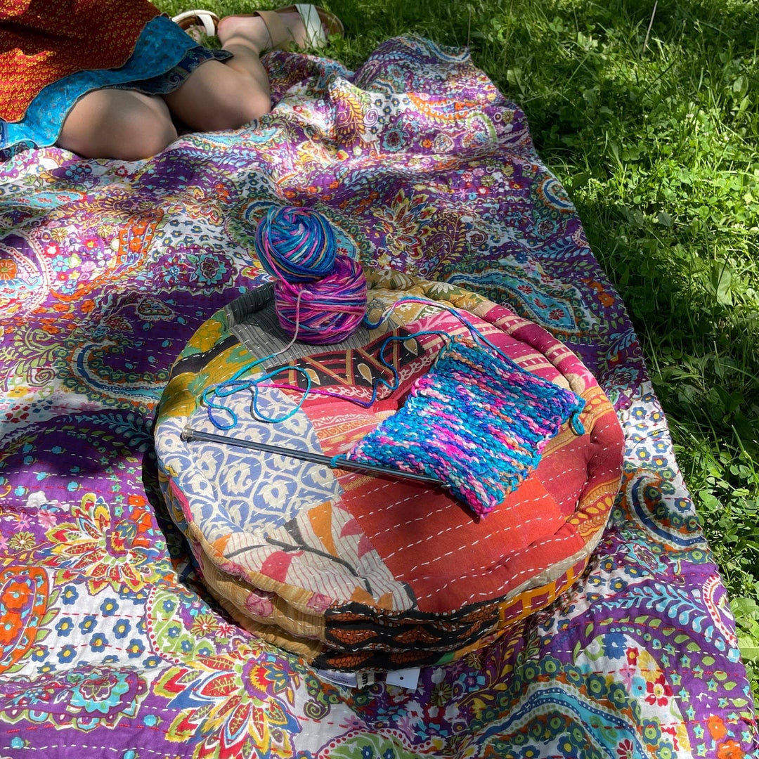 One of a Kind Hand Embroidered Pouf sitting on a picnic blanket with yarn and knitting needles on top.