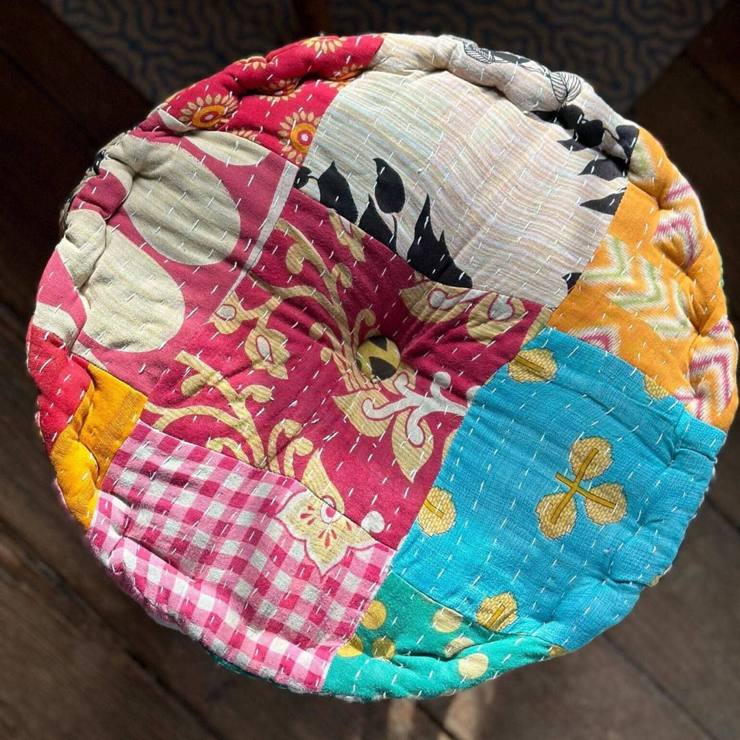 An above view of a patchwork embroidered Pouf Pillow. This pattern has pinks, reds blues and blacks