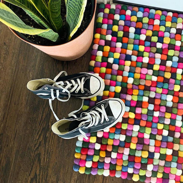 Felt ball rug as a doormat with black sneakers sitting on top.