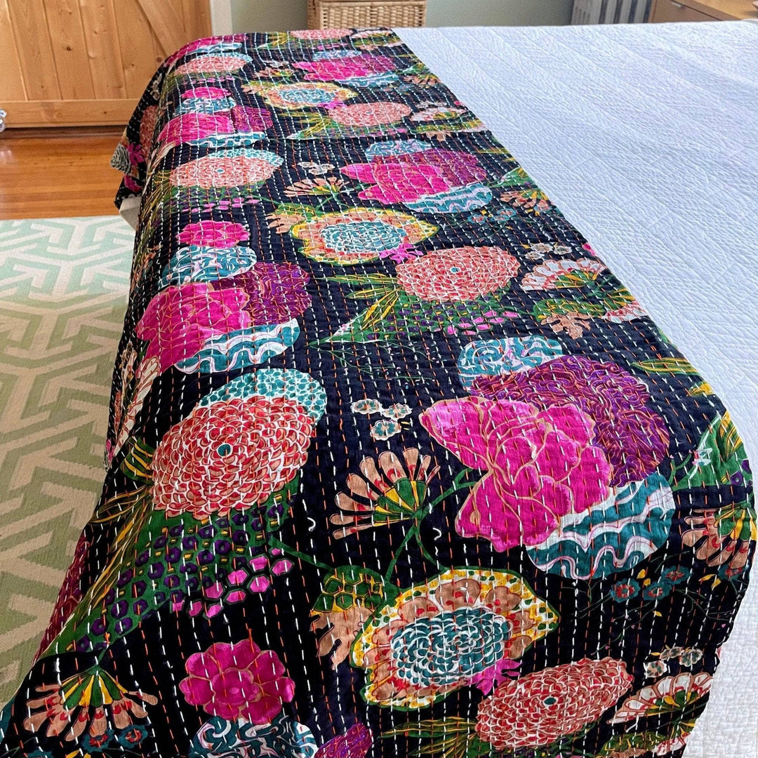 Night Lily Kantha quilt laying at the end of a bed with white bedding underneath. 