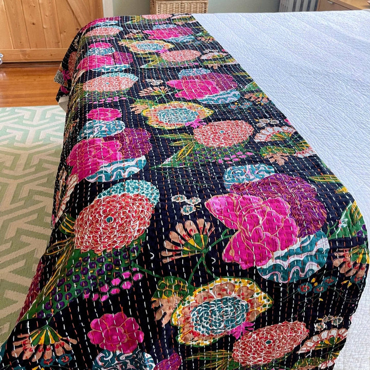 Night Lily Kantha quilt laying at the end of a bed with white bedding underneath. 