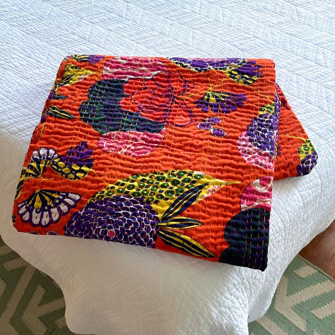 Orange Symphony kantha quilt at the age of a bed folded into a square on top of white bedding 
