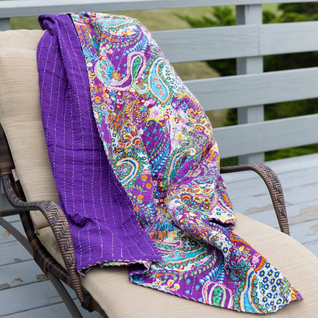 Purple kantha quilt blanket laying on a deck chair outside 
