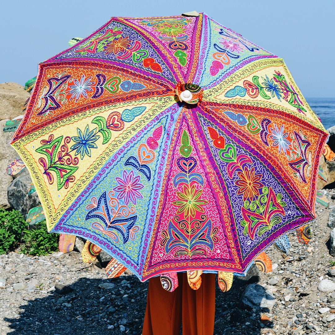 Model is holding the one of a kind handmade beach umbrella over their shoulder. We see the top of the umbrella fanned out with all it's colorful designs. 